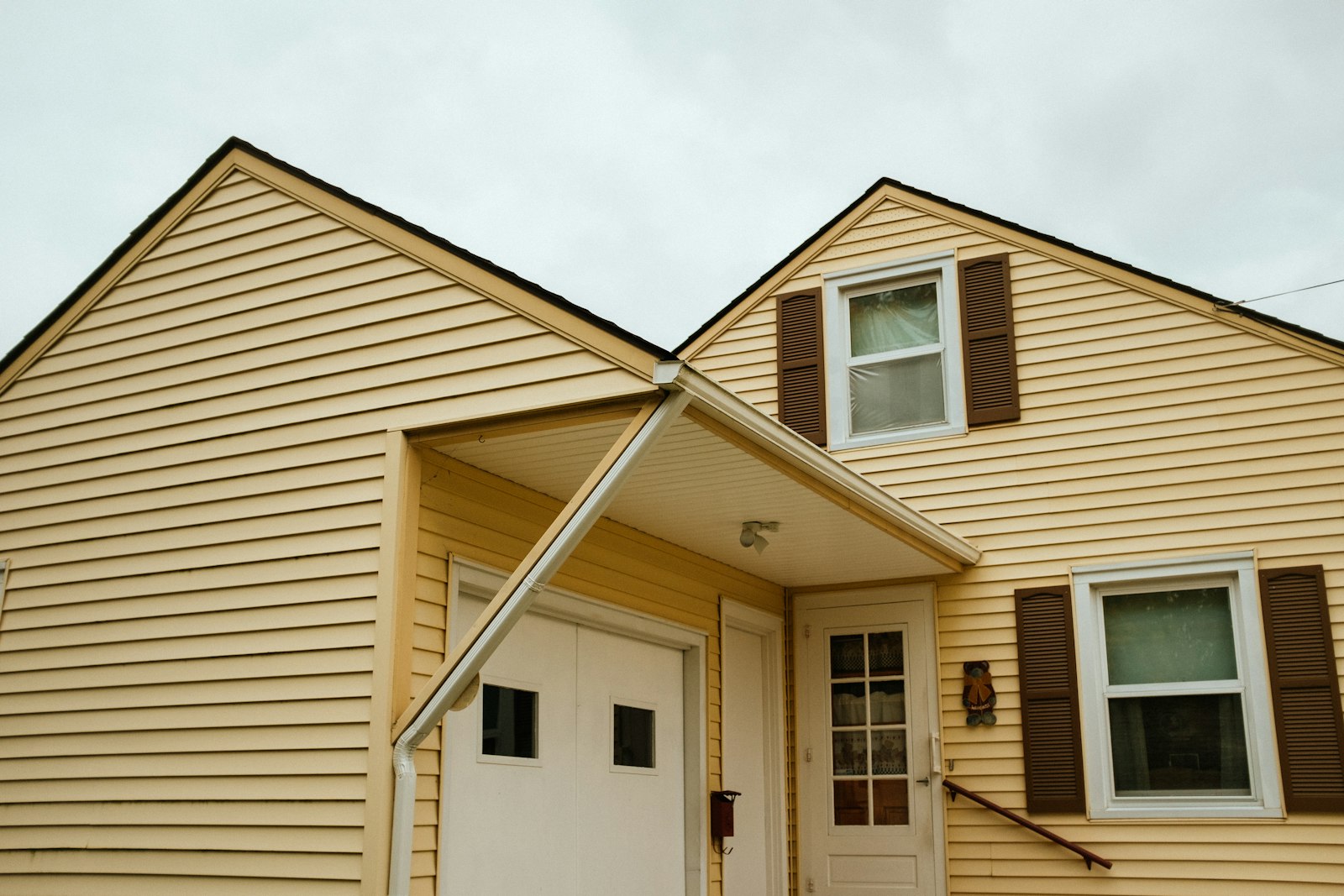 Yellow vinyl lap siding on a two story Midwest home with brown shutters, white trim and a downspout