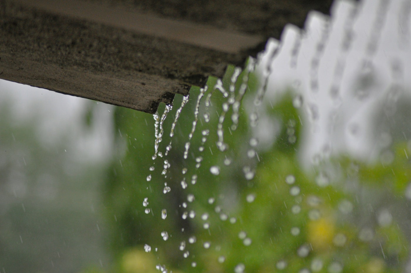 Rainwater streaming off a roof edge during a heavy downpour instead of being carried away by the gutter